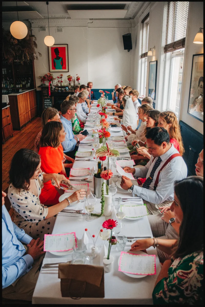 Guests read pink-edged menus along a long white table with orange gerberas in the upstairs room at Camberwell Arms