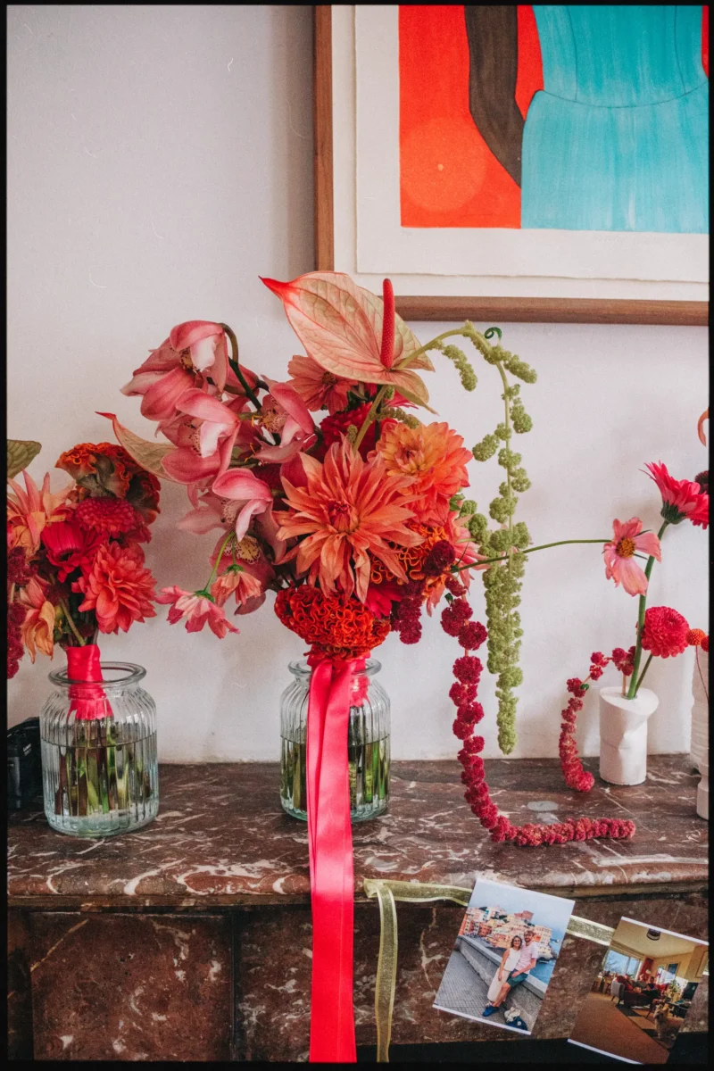 Pink and coral flowers with a red ribbon in ribbed glass jars under a teal and orange print at Camberwell Arms