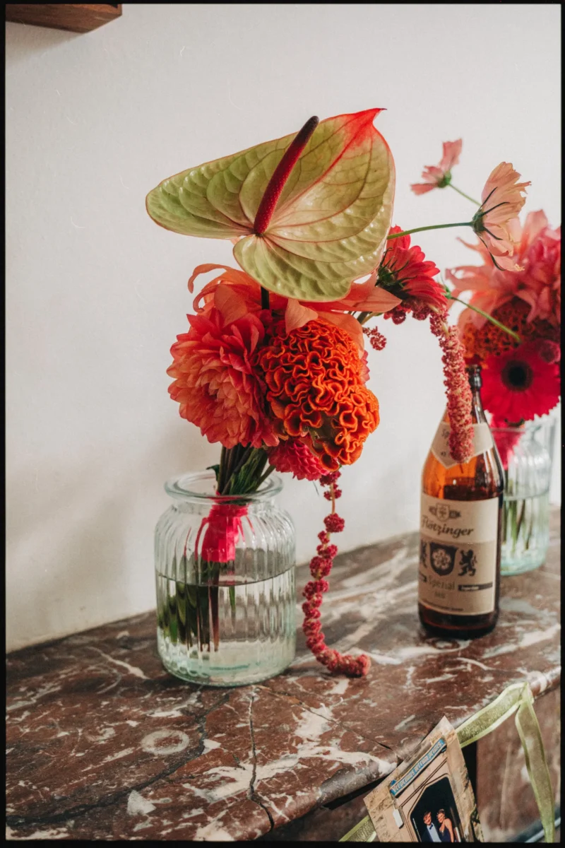 Pale green anthurium and frilly orange cockscomb in a ribbed jar beside a beer bottle at Camberwell Arms
