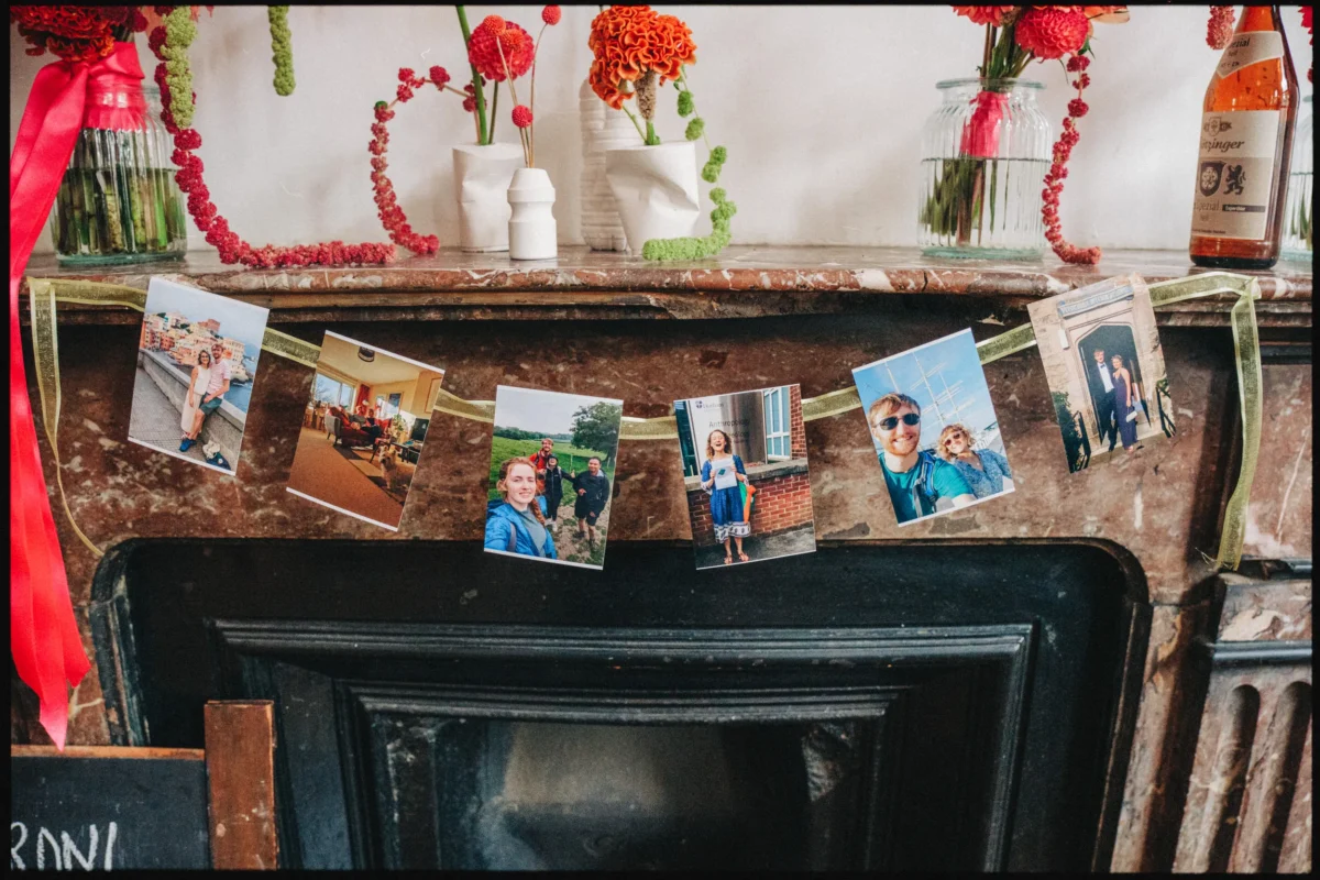 Printed snapshots hung on gold ribbon across a marble mantelpiece with red and orange flowers at Camberwell Arms