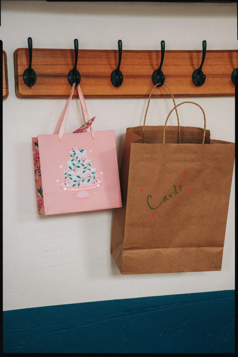 Pink Congratulations gift bag and a kraft paper bag hand-lettered Cards hanging from black hooks on a wooden rail