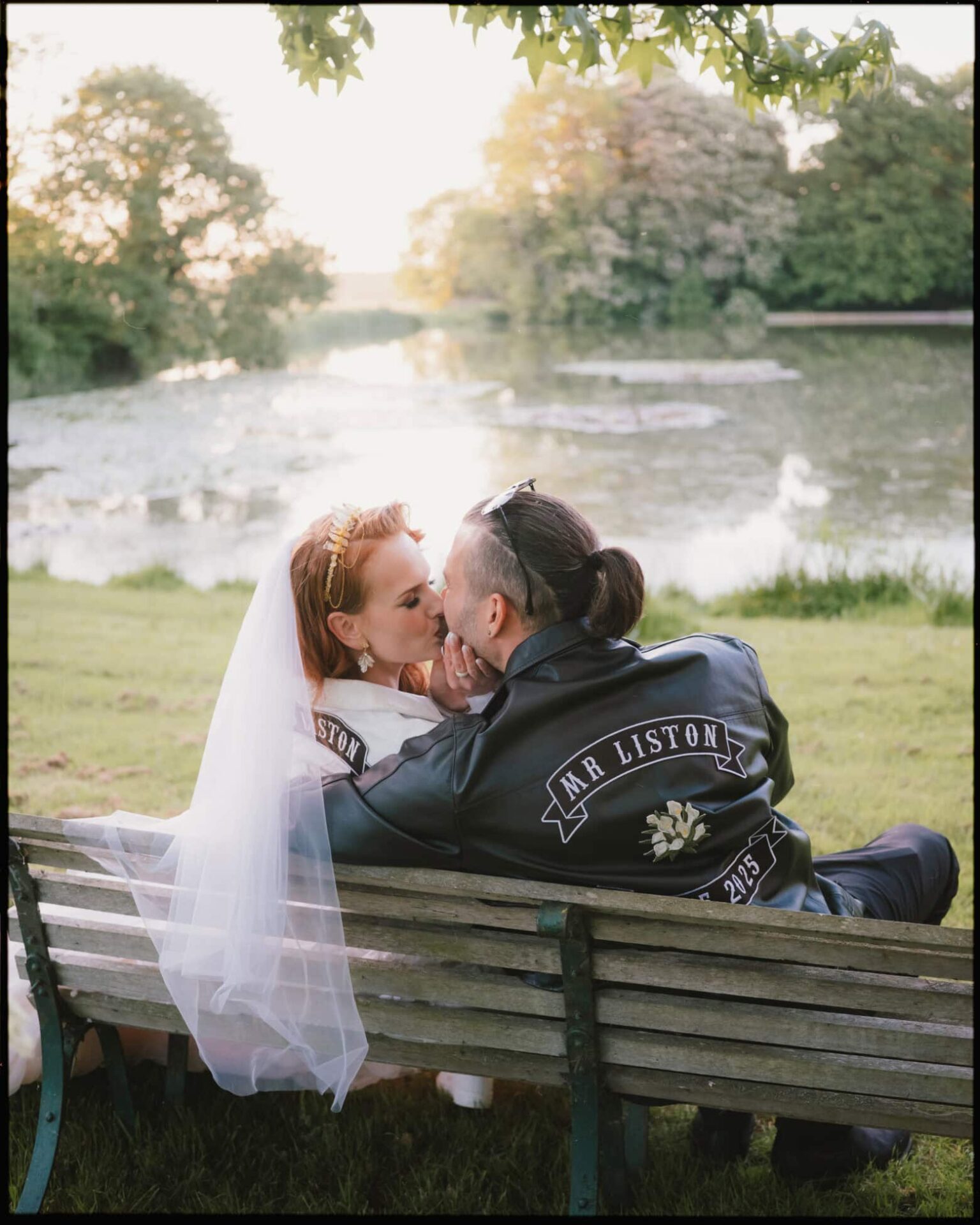Golden hour by the lake at Preston Court — the couple in matching jackets sharing a quiet kiss as the sun sets. Newlyweds sharing a kiss by the lake at Preston Court during golden hour, wearing matching personalised jackets