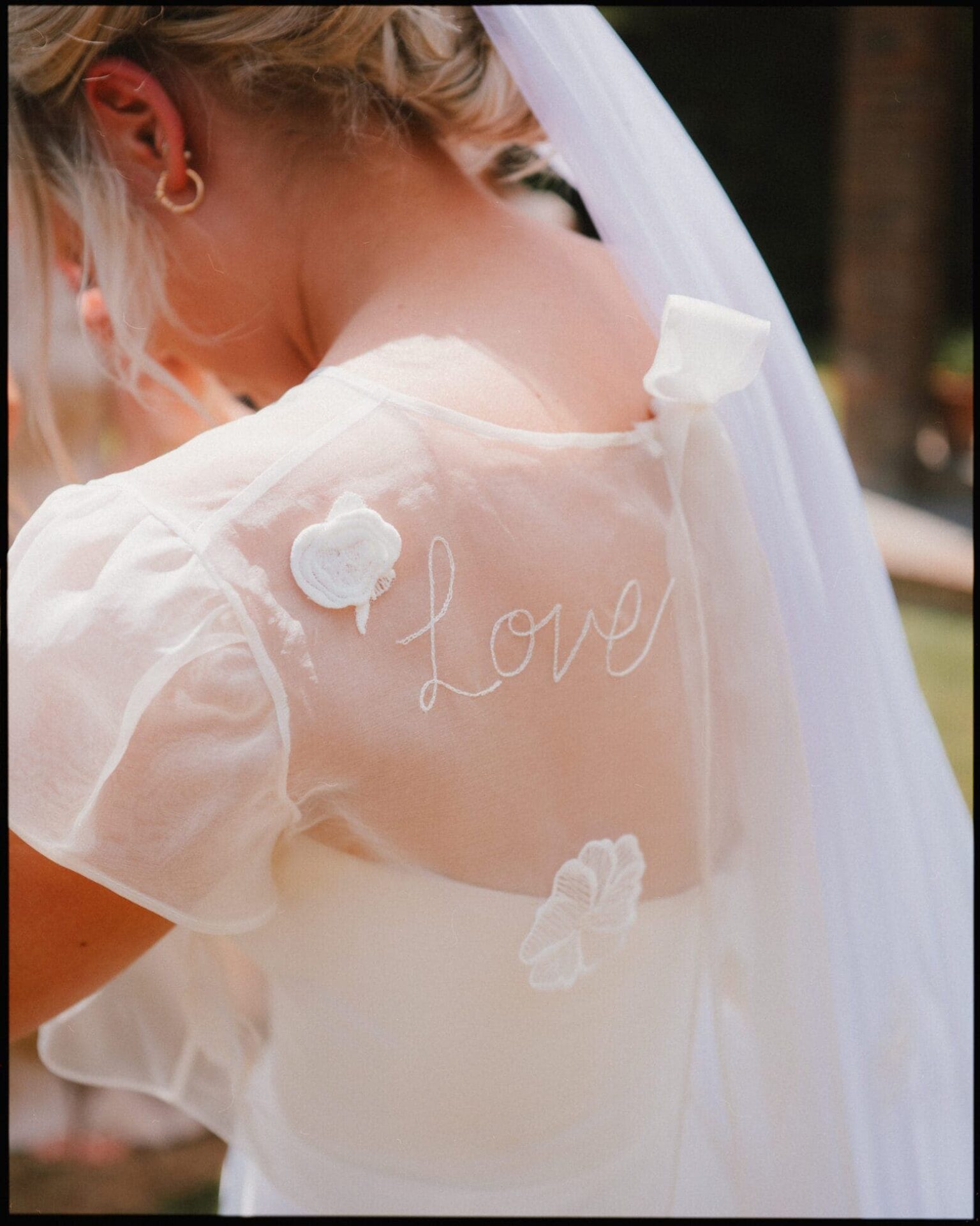 A delicate detail from the morning at Longton Wood in Kent — the bride’s dress embroidered with the word “Love” as she prepares for her woodland wedding ceremony. Close-up of bride’s embroidered lace dress with the word “Love” as she prepares for her wedding ceremony at Longton Wood in Kent.